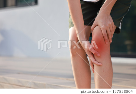 Close up of woman standing and holding her painful knee with red highlight. Sport injury, ligament tear, runner's knee and joint inflammation concept for health care and physical therapy. Close up of woman standing and holding her painful knee with red highlight. Sport injury, ligament tear, runner's knee and joint inflammation concept for health care and physical therapy. 137838804