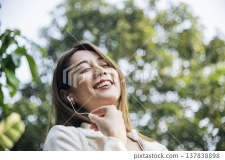 Happy asian woman use headphones listen to music from smartphone outdoor in green park nature. Music mental therapist for relaxation woman. Leisure cheerful wellness woman smile sitting in green park Happy asian woman use headphones listen to music from smartphone outdoor in green park nature. Music mental therapist for relaxation woman. Leisure cheerful wellness woman smile sitting in green park 137838898