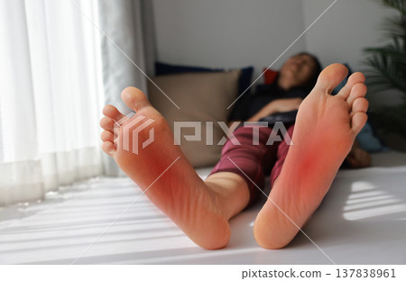 Woman sitting and massaging both of her painful feet with red highlight on soles. Foot pain, plantar fasciitis, overused feet and peripheral neuropathy concept for health care and therapy. Woman sitting and massaging both of her painful feet with red highlight on soles. Foot pain, plantar fasciitis, overused feet and peripheral neuropathy concept for health care and therapy. 137838961