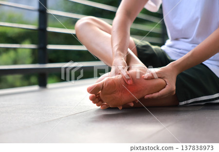 Woman sitting and massaging both of her painful feet with red highlight on soles. Foot pain, plantar fasciitis, overused feet and peripheral neuropathy concept for health care and therapy. Woman sitting and massaging both of her painful feet with red highlight on soles. Foot pain, plantar fasciitis, overused feet and peripheral neuropathy concept for health care and therapy. 137838973