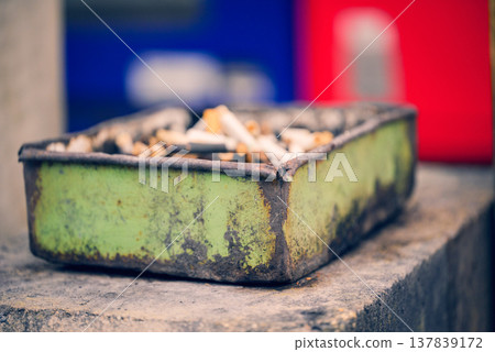 A rusty ashtray and a pile of cigarette butts A rusty ashtray and a pile of cigarette butts 137839172