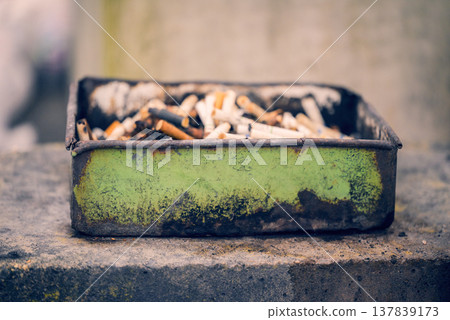 A rusty ashtray and a pile of cigarette butts A rusty ashtray and a pile of cigarette butts 137839173