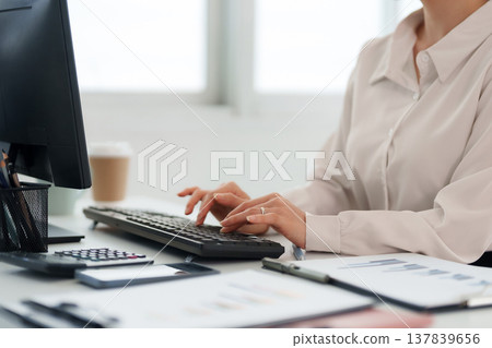 Adult professional typing on computer keyboard analyzing business reports and financial data for productivity in modern office environment 137839656
