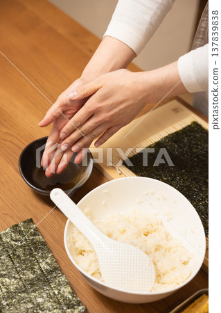 Close-up of a woman's hands making Ehomaki (lucky direction sushi roll). Close-up of a woman's hands making Ehomaki (lucky direction sushi roll). 137839838