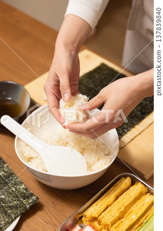 Close-up of a woman's hands making Ehomaki (lucky direction sushi roll). Close-up of a woman's hands making Ehomaki (lucky direction sushi roll). 137839840