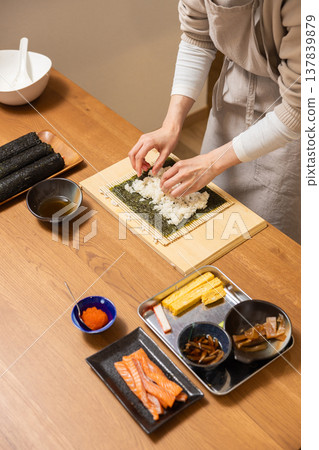 Close-up of a woman's hands making Ehomaki (lucky direction sushi roll). Close-up of a woman's hands making Ehomaki (lucky direction sushi roll). 137839879