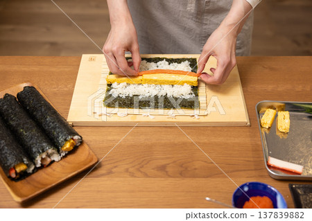 Close-up of a woman's hands making Ehomaki (lucky direction sushi roll). Close-up of a woman's hands making Ehomaki (lucky direction sushi roll). 137839882
