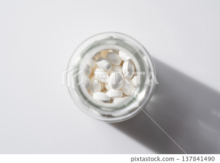 An overhead photograph of white pills in a bottle placed against a white background. 137841490