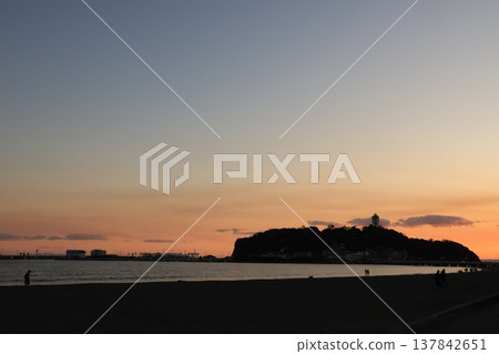 The scenery around Enoshima Island, bathed in orange light as seen from Koshigoe Beach at sunset. The scenery around Enoshima Island, bathed in orange light as seen from Koshigoe Beach at sunset. 137842651