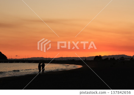 The scenery around Enoshima Island, bathed in orange light as seen from Koshigoe Beach at sunset. The scenery around Enoshima Island, bathed in orange light as seen from Koshigoe Beach at sunset. 137842656