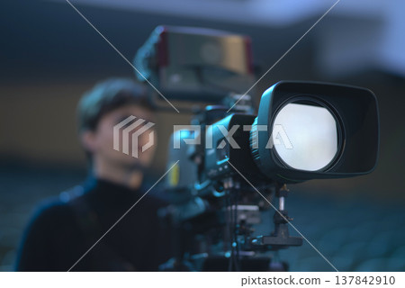 Professional video camera lens with white light reflection and blurred filmmaker with copy space 137842910