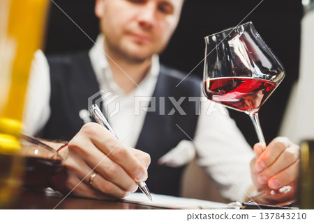Man fills in paper form holding delicious red wine at table 137843210