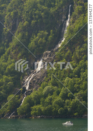 Scenic waterfall in Norwegian fjord with small white motorboat and copy space 137844277