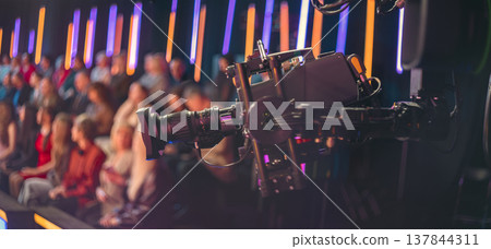 Professional broadcast camera filming live TV show with blurred audience and copy space Professional broadcast camera filming live TV show with blurred audience and copy space 137844311