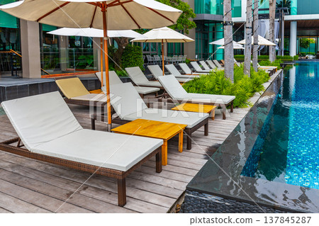 Rows of poolside chairs with an umbrella for sitting, lying down, relaxing and sunbathing. Rows of poolside chairs with an umbrella for sitting, lying down, relaxing and sunbathing. 137845287
