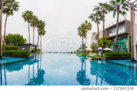 seaside pool with sun loungers and tall palm trees as decoration and a modern building for relaxation. seaside pool with sun loungers and tall palm trees as decoration and a modern building for relaxation. 137845334