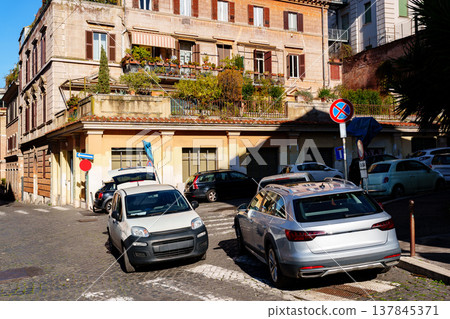 Cars parked on a quiet street near buildings with plants in an urban area at midday Cars parked on a quiet street near buildings with plants in an urban area at midday 137845371
