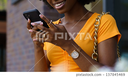 Young person with phone smiling outside during daytime in a city area Young person with phone smiling outside during daytime in a city area 137845469