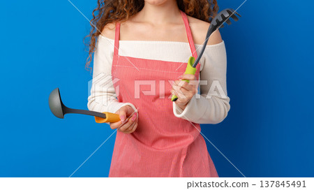 Woman holds kitchen and gardening tools with a blue background during day Woman holds kitchen and gardening tools with a blue background during day 137845491