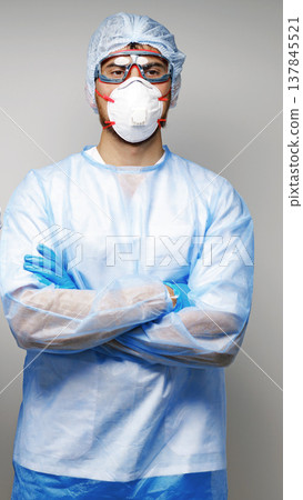 Healthcare worker stands with arms crossed while wearing protective gear in a clinical setting 137845521