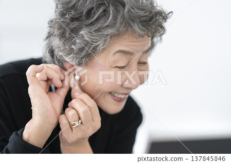 一位面帶微笑的老婦人對著鏡子戴耳環。 一位面帶微笑的老婦人對著鏡子戴耳環。 137845846