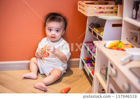 A cute little child smiles happily while playing with toys made from wood and non-toxic paint to enhance their development. A cute little child smiles happily while playing with toys made from wood and non-toxic paint to enhance their development. 137846319
