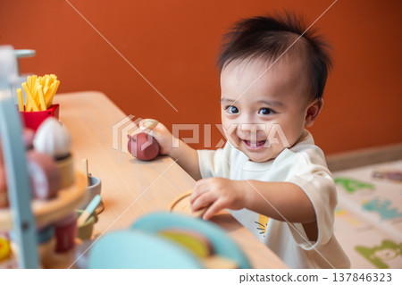 A cute little child smiles happily while playing with toys made from wood and non-toxic paint to enhance their development. A cute little child smiles happily while playing with toys made from wood and non-toxic paint to enhance their development. 137846323