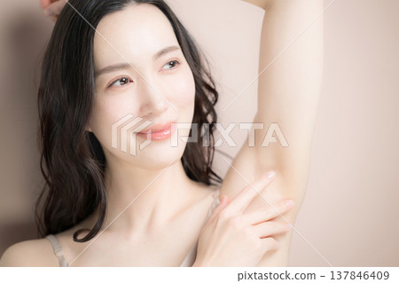 特寫鏡頭展示了年輕女性的腋下美容護理和美學，例如脫毛，背景是粉米色。 137846409