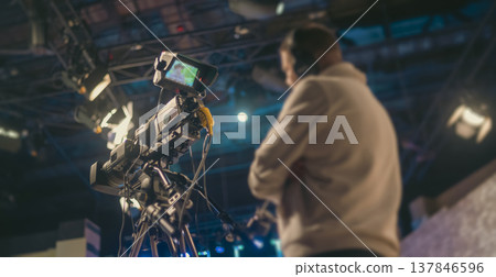 Professional TV camera in studio filming broadcast with cameraman on background and copy space Professional TV camera in studio filming broadcast with cameraman on background and copy space 137846596