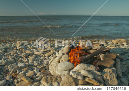 Warm Campfire in Stone Hearth on Pebble Beach at Sunset with Copy Space Warm Campfire in Stone Hearth on Pebble Beach at Sunset with Copy Space 137846616