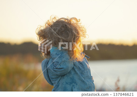 Curly Little Child Looking at Sunset Outdoors with Soft Backlight and copy space 137846621