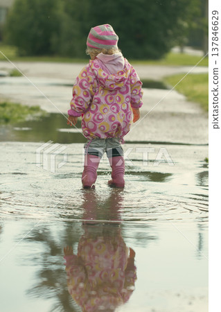 Toddler in pink raincoat standing in puddle with reflection and copy space 137846629