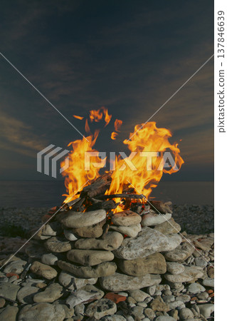 Burning campfire in stone pit on pebble beach by the sea at twilight with copy space 137846639