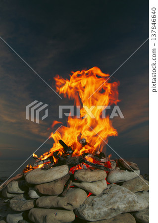 Dynamic campfire flame in stone fire pit on the beach at twilight with copy space 137846640