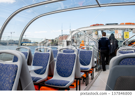 Passengers can enjoy the spacious interior of a stylish boat with ergonomic seating as crew members get ready to depart from the docks on a sunny day. Passengers can enjoy the spacious interior of a stylish boat with ergonomic seating as crew members get ready to depart from the docks on a sunny day. 137846800
