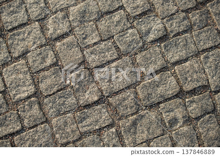 Close-up view of rugged cobblestone pavement laid in a patterned formation, set in an urban environment under natural light. 137846889