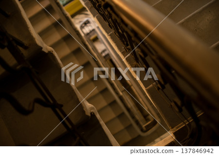 Looking down a spiral staircase in a historic building, showcasing intricate railings and soft light illuminating the steps below Looking down a spiral staircase in a historic building, showcasing intricate railings and soft light illuminating the steps below 137846942