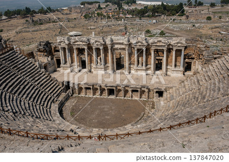 Explore the stunning ancient theatre at Pamukkale, showcasing intricate architecture and rich history, nestled among the ruins of an ancient settlement. 137847020
