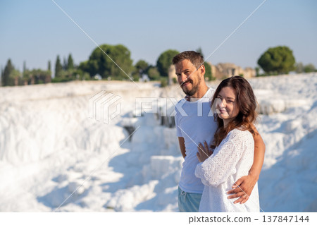 Beautiful couple stands together at Pamukkale, admiring the stunning white travertine terraces and warm thermal waters in a sunny, serene setting. Beautiful couple stands together at Pamukkale, admiring the stunning white travertine terraces and warm thermal waters in a sunny, serene setting. 137847144