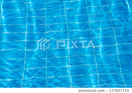 Sunlight glistens on the surface of a swimming pool, creating a vibrant display of blue tones and a grid of lines visible beneath the water. 137847159