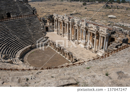 Tourists admire the well-preserved ruins of the ancient theater in Pamukkale, showcasing impressive columns and expansive seating in a historical context. Tourists admire the well-preserved ruins of the ancient theater in Pamukkale, showcasing impressive columns and expansive seating in a historical context. 137847247