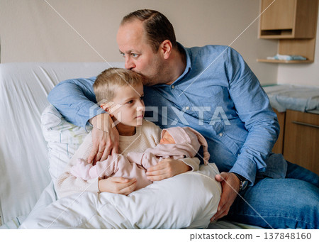 Father kissing older son while holding newborn baby girl. Emotional family moment showing love and connection between siblings. Father kissing older son while holding newborn baby girl. Emotional family moment showing love and connection between siblings. 137848160