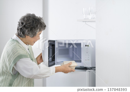 Senior woman heating food in a microwave Senior woman heating food in a microwave 137848393