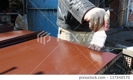 A painter covers a sheet of iron lying on the surface of a workbench with brown paint to prevent rust when using metal material in the household, applying protective paint to an iron product outdoors A painter covers a sheet of iron lying on the surface of a workbench with brown paint to prevent rust when using metal material in the household, applying protective paint to an iron product outdoors 137848570