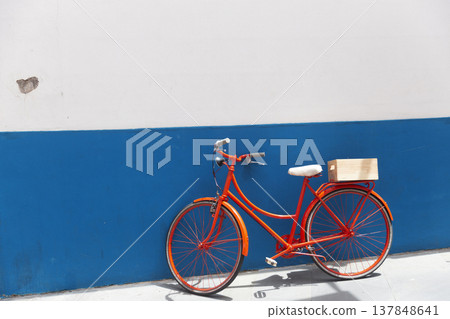 Bright orange vintage bicycle parked against blue and white minimalist wall with vast copy space 137848641