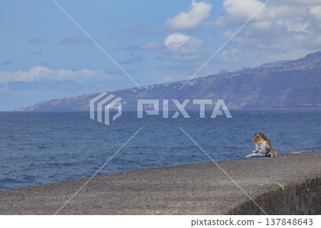 Two young women sitting on pier admiring vast ocean and coastline with copy space 137848643