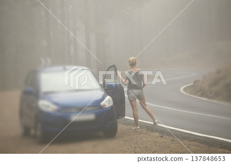 Woman traveler standing by car on a winding foggy mountain road with copy space in fog 137848653
