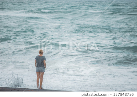 Lonely woman standing on beach looking at powerful turquoise ocean waves with copy space Lonely woman standing on beach looking at powerful turquoise ocean waves with copy space 137848756