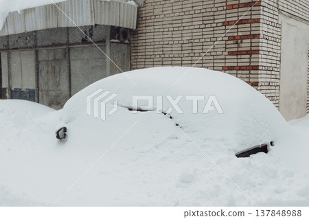 Parking of cars covered with snow. Heavy snowfall covered the road. Car in the snow. Consequences of a snowstorm.Abandoned car on the side of the road. 137848988