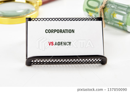 A crisp white card, bearing CORPORATION VS AGENCY in bold text, rests on a bright desk A crisp white card, bearing CORPORATION VS AGENCY in bold text, rests on a bright desk 137850090